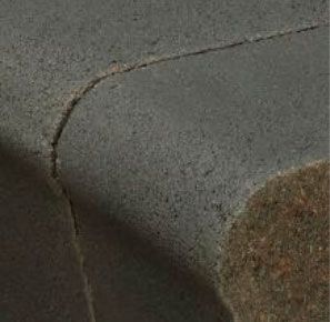 Cracked asphalt curb and road surface, bordering dry grass.