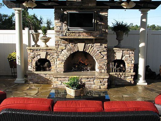 Outdoor stone fireplace with a built-in TV, flanked by white columns and seating.