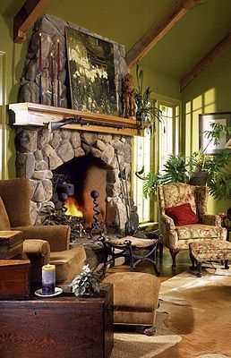 Stone fireplace in living room with armchairs, fire burning, artwork, and plants.