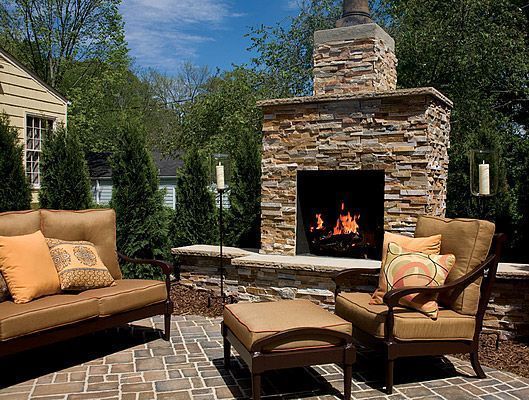 Outdoor patio with stone fireplace, seating area with sofa, chair, and ottoman.