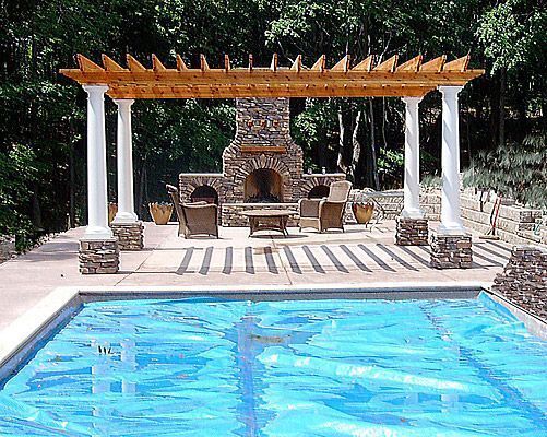 Pool with blue cover, pergola with fireplace, patio furniture, and white columns.