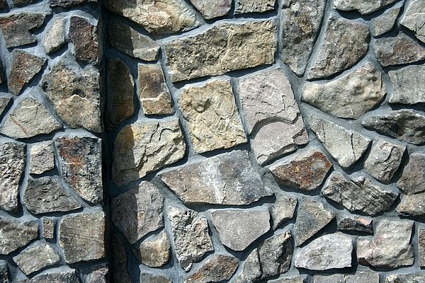 Stone wall with gray mortar; stones are tan and gray.