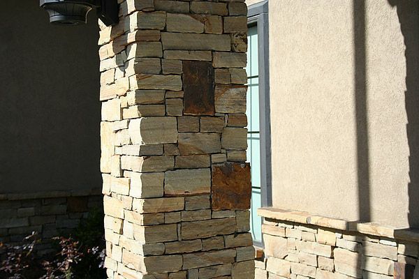 Stone-covered pillar next to a window on a beige stucco wall, in natural sunlight.