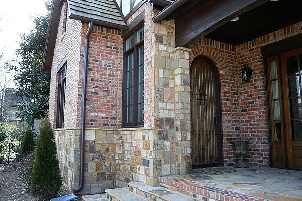 Brick and stone exterior of a house with a wooden arched doorway and windows.