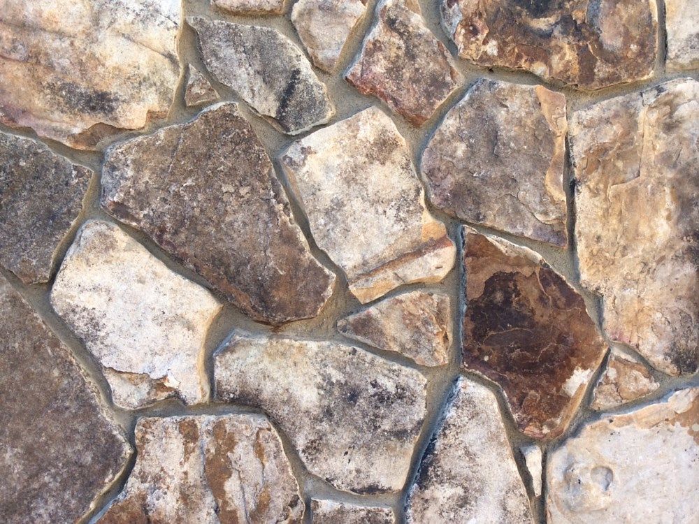 Close-up of a stone wall with irregular, multi-toned brown and beige stones and gray mortar.