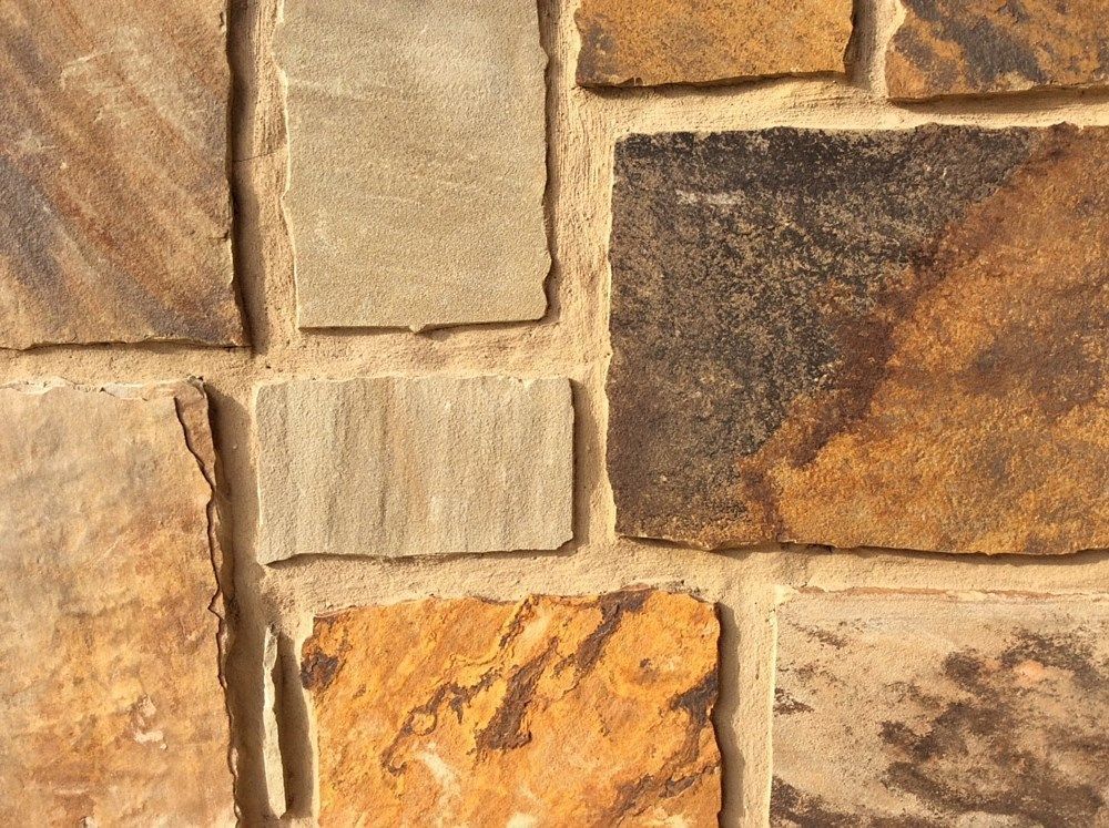 Stone wall with varied rectangular and square blocks in shades of brown and tan, mortar in between.