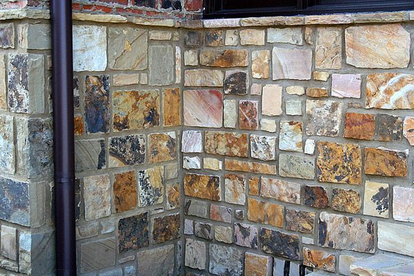 Stone veneer wall in shades of brown, tan, and gray, with a dark brown gutter.