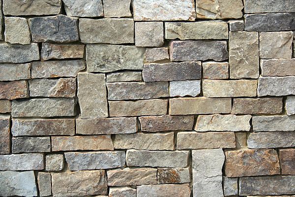 Stone wall with rectangular blocks in shades of tan, brown, and gray.