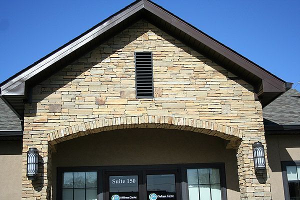 Stone facade entrance to a building with dark-framed windows, arch, and a brown roof.