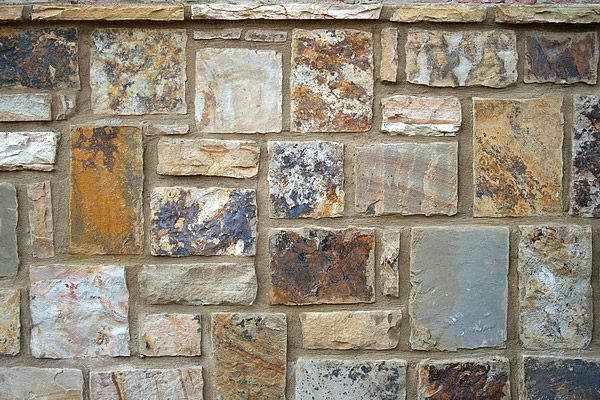 Stone wall with various rectangular and square-shaped stones in earthy tones, mortared together.
