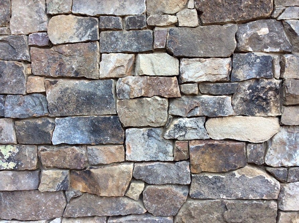 Stone wall composed of various earthy-toned rectangular and irregular stones.