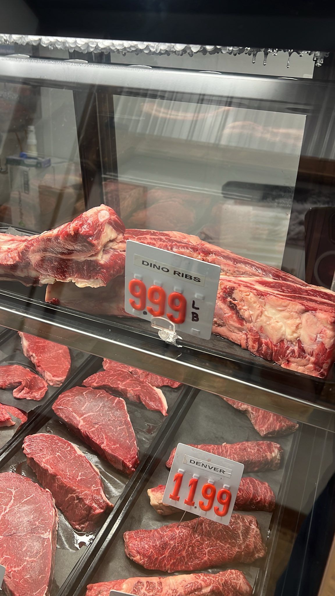 Meat display with price tags. Top: large cut for $9.99/lb. Bottom: steaks for $11.99/lb.