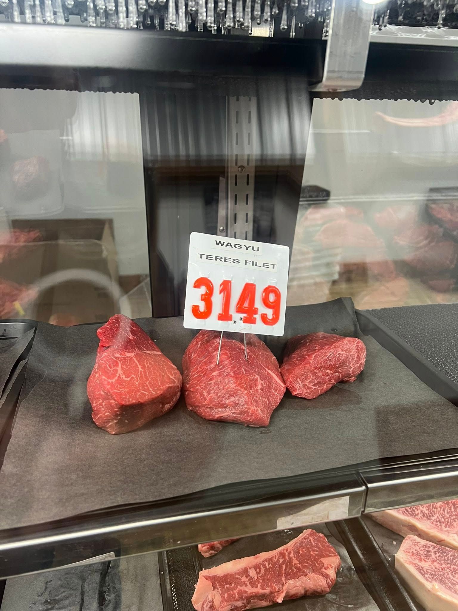 Three raw beef steaks displayed in a refrigerated case with a price tag of $31.49.