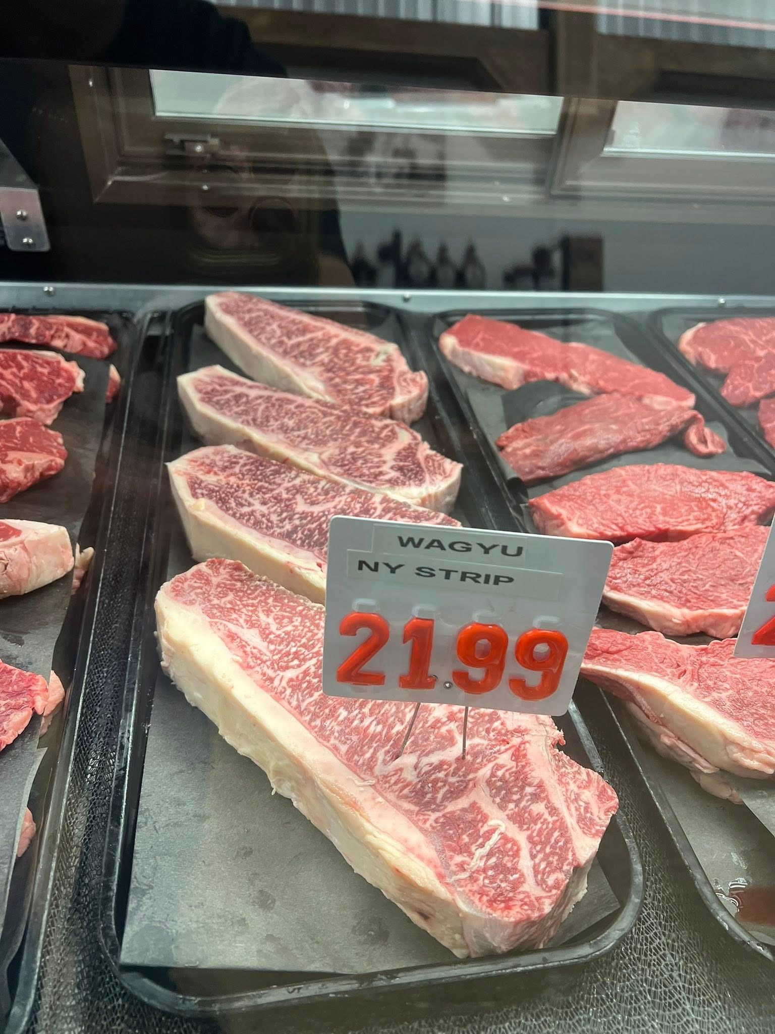 Wagyu NY strip steaks in a refrigerated display case, priced at $21.99.