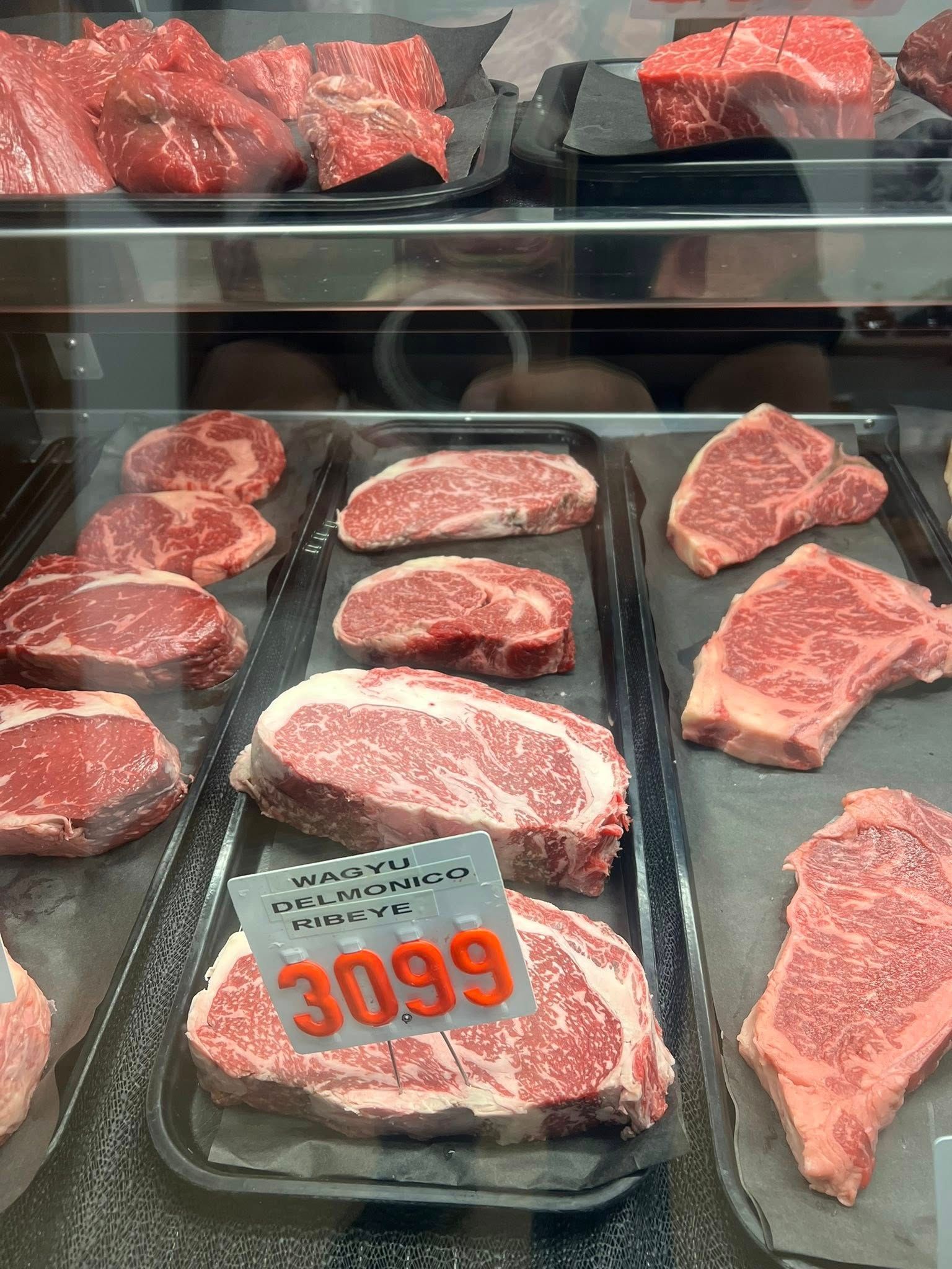 Display case with various cuts of raw beef steaks, some with prominent marbling, price tag visible: $30.99.