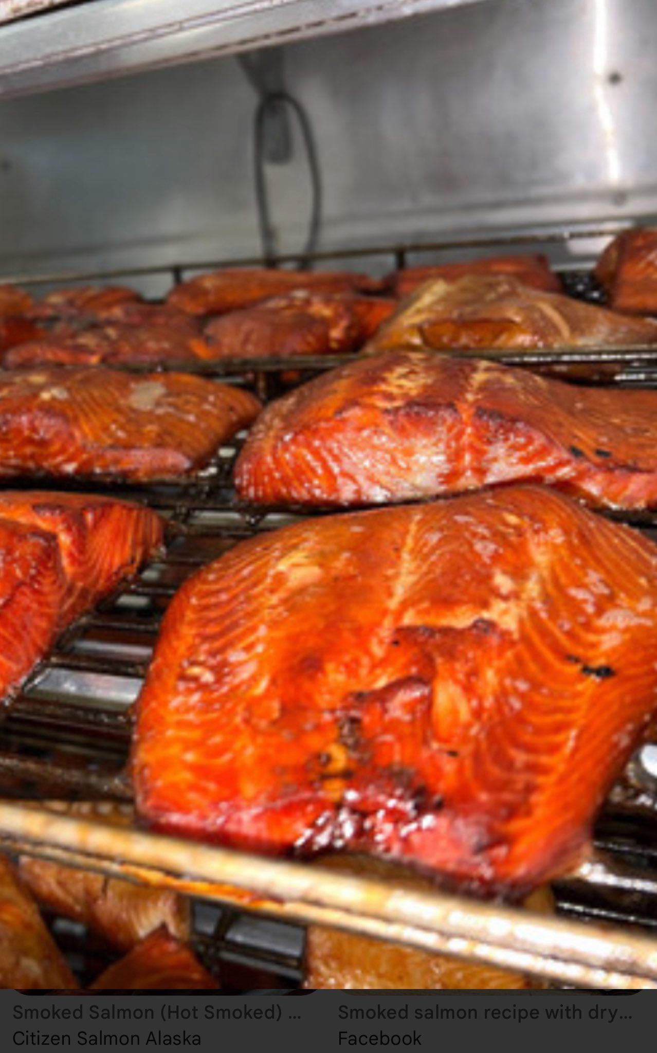 Smoked salmon fillets on metal racks inside a smoker, reddish-brown color.
