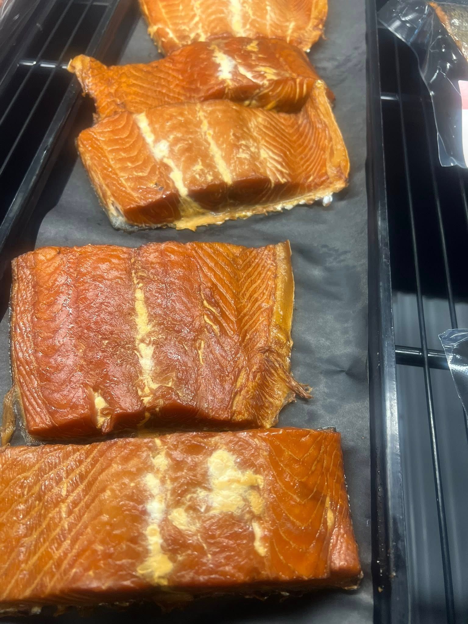 Smoked salmon fillets, shades of brown, displayed in a store tray.