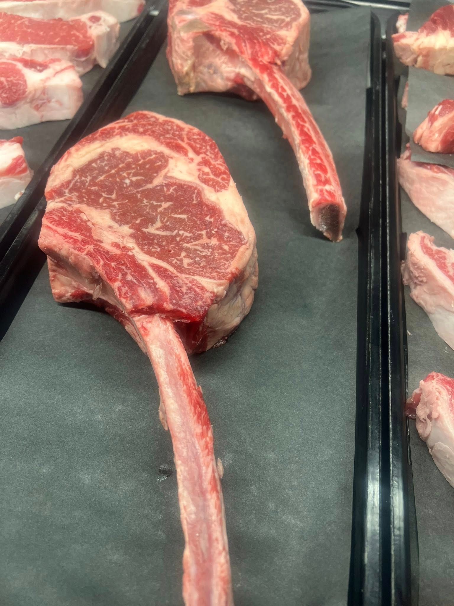 Raw tomahawk steaks on display in a butcher shop, red meat with bone.