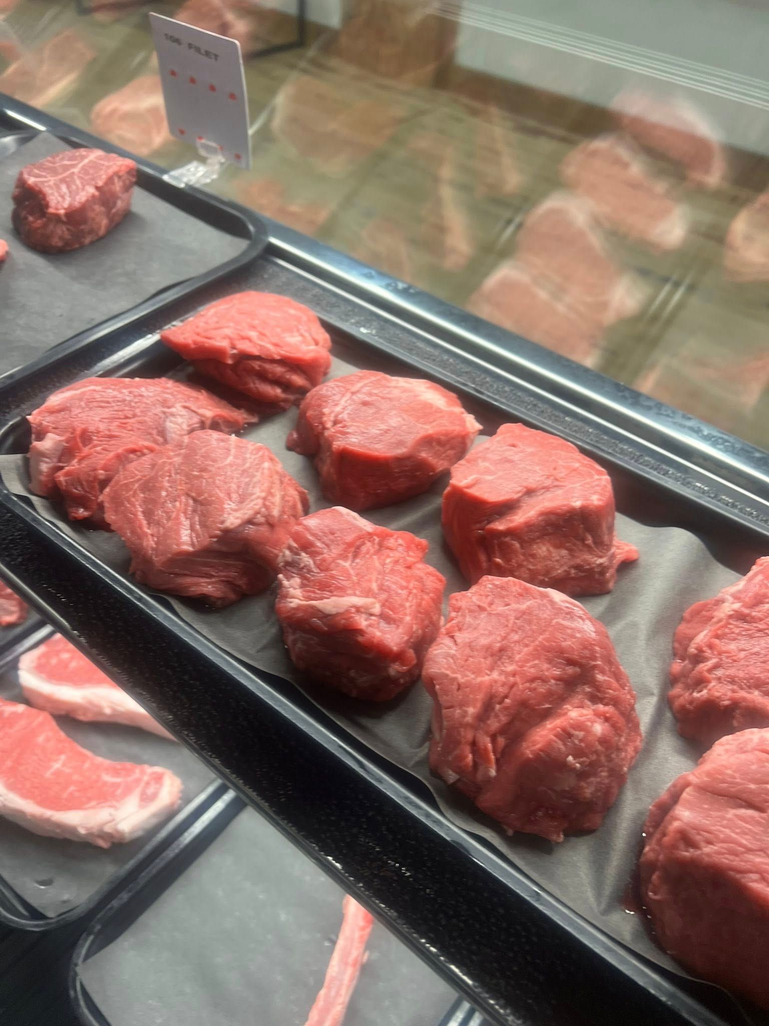 Display case of raw, red beef tenderloin steaks on trays.