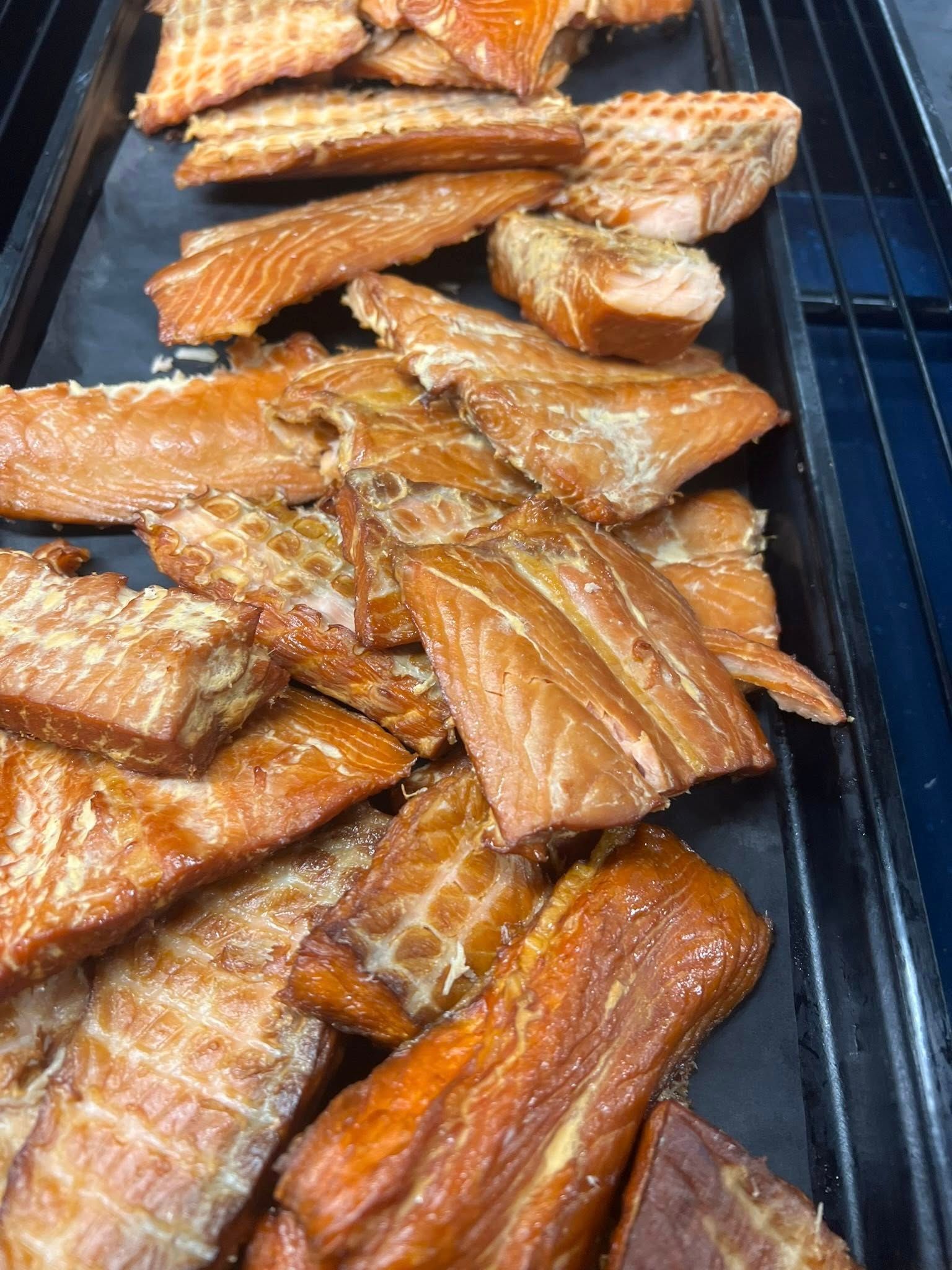 Smoked salmon fillets, various sizes, displayed on a black surface. Brown and reddish hues.
