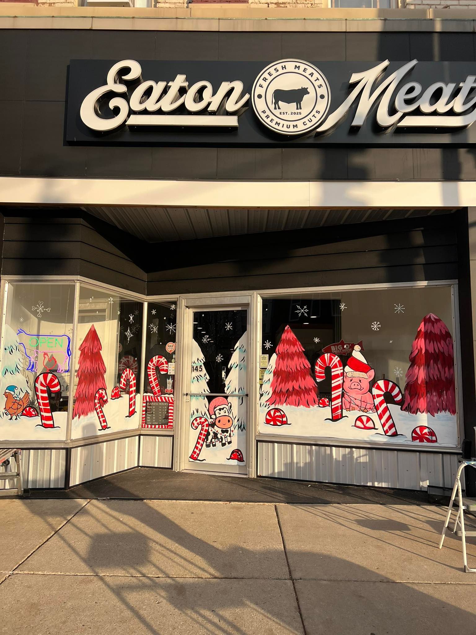 Exterior of Eaton Meats store with festive Christmas window decorations, including red trees and candy canes.