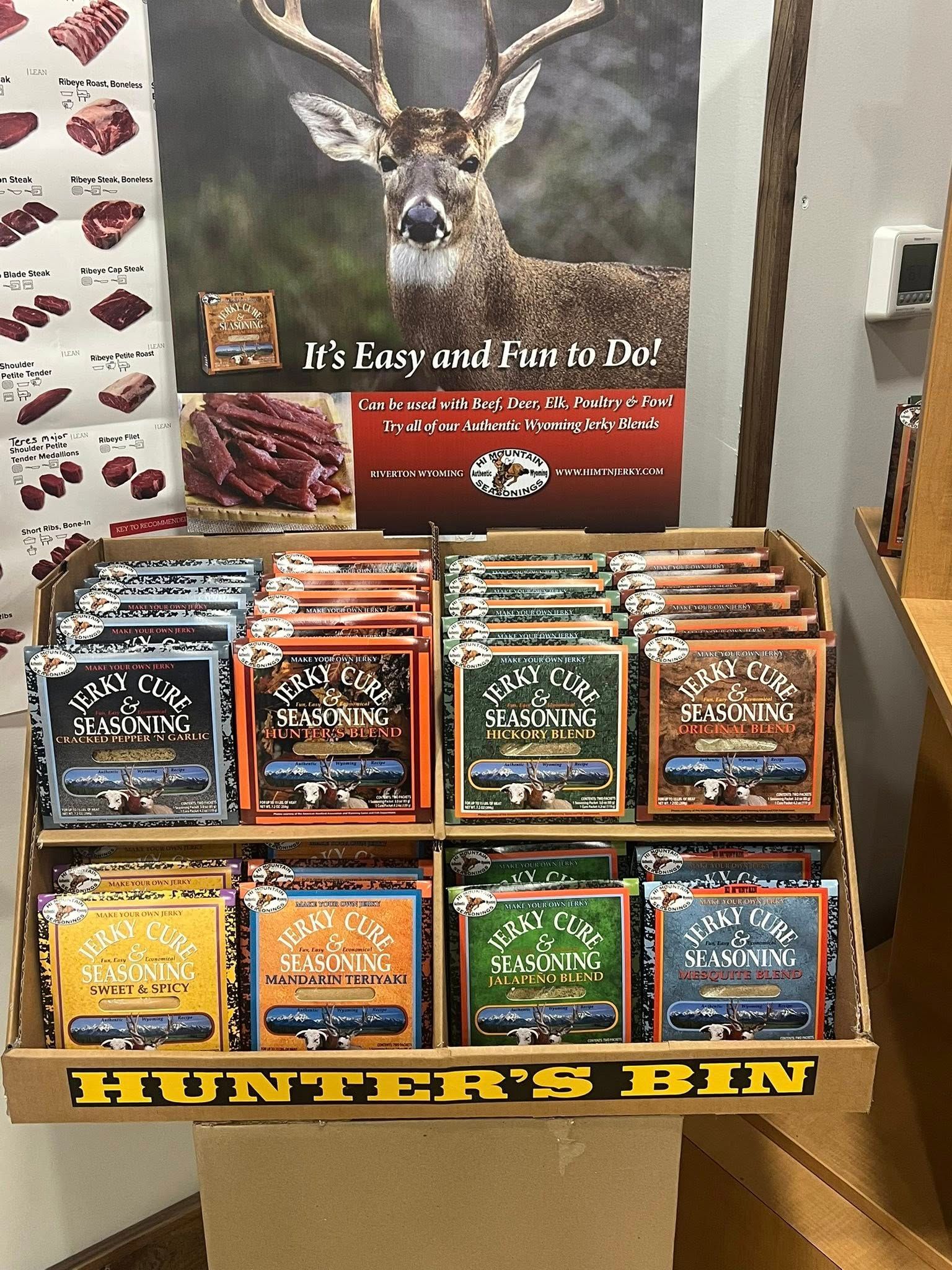 Display of Hunter's Bin jerky with deer poster in a store. Packs of jerky are arranged in rows.