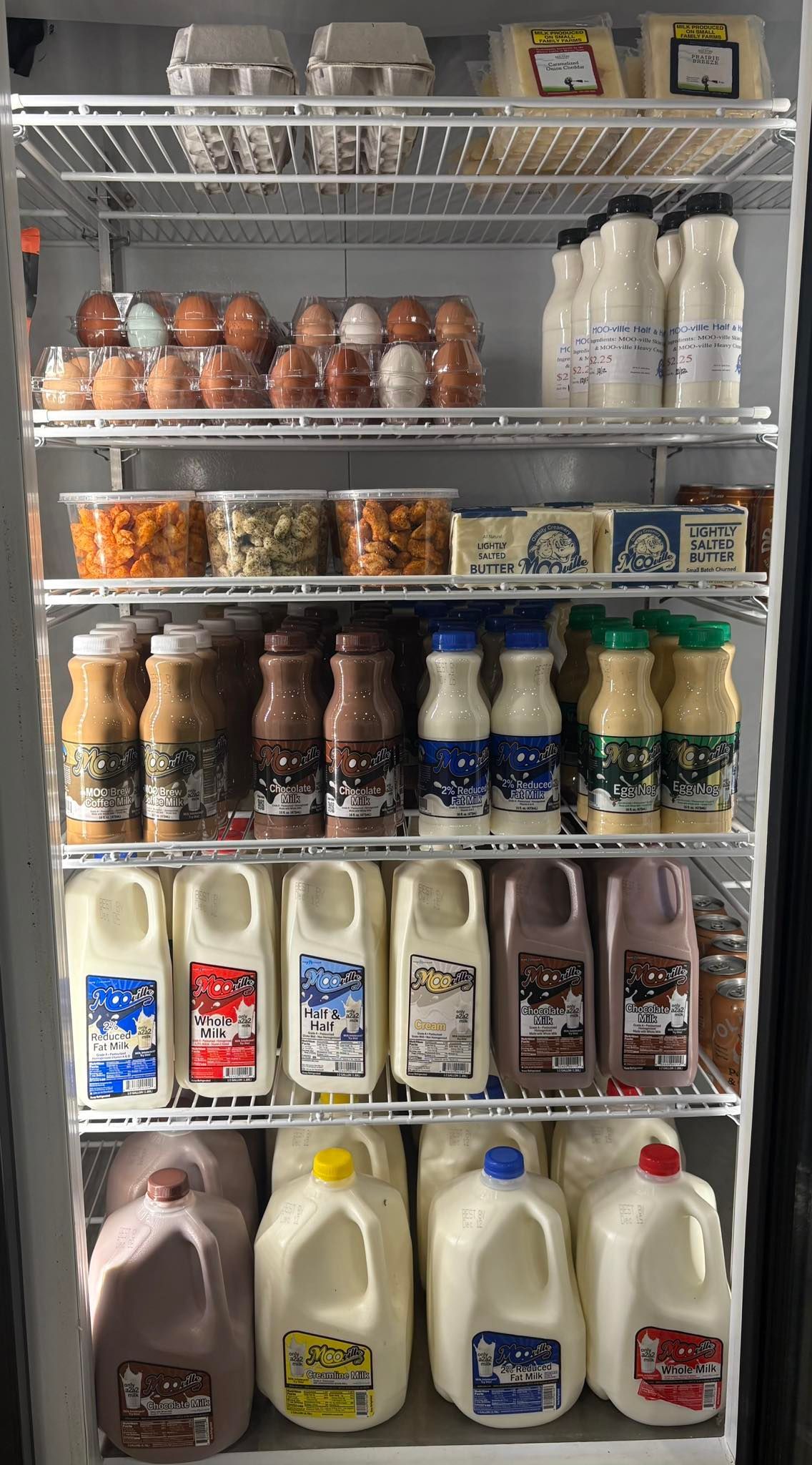 Refrigerator shelves filled with cartons of eggs, milk, drinks, and snacks.