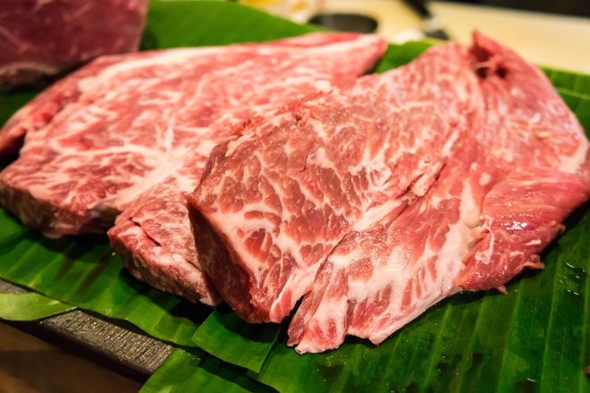 Raw, marbled beef steaks on green banana leaves.