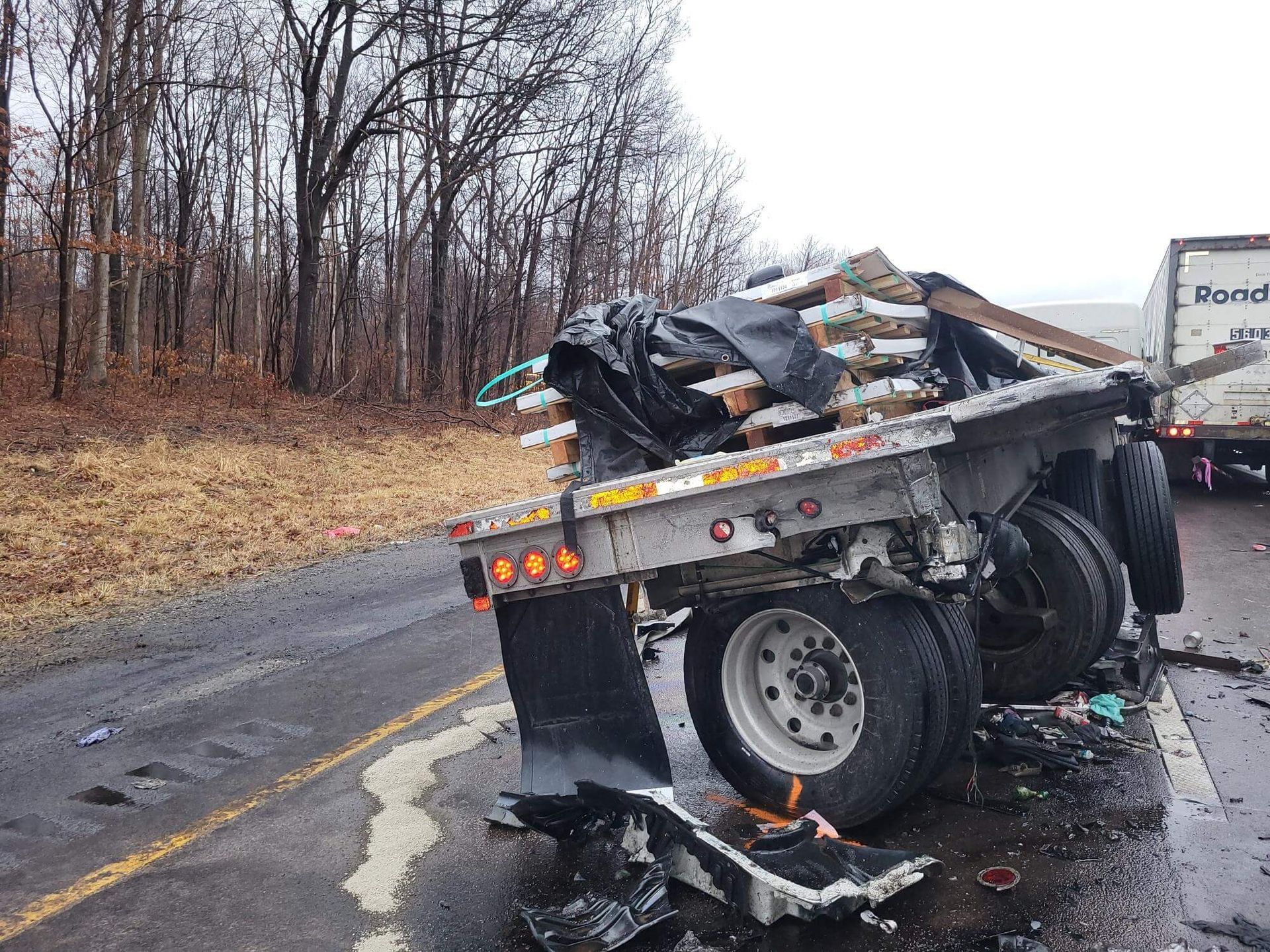 Damaged truck on a wet road after a crash, with debris and trees lining the roadside.