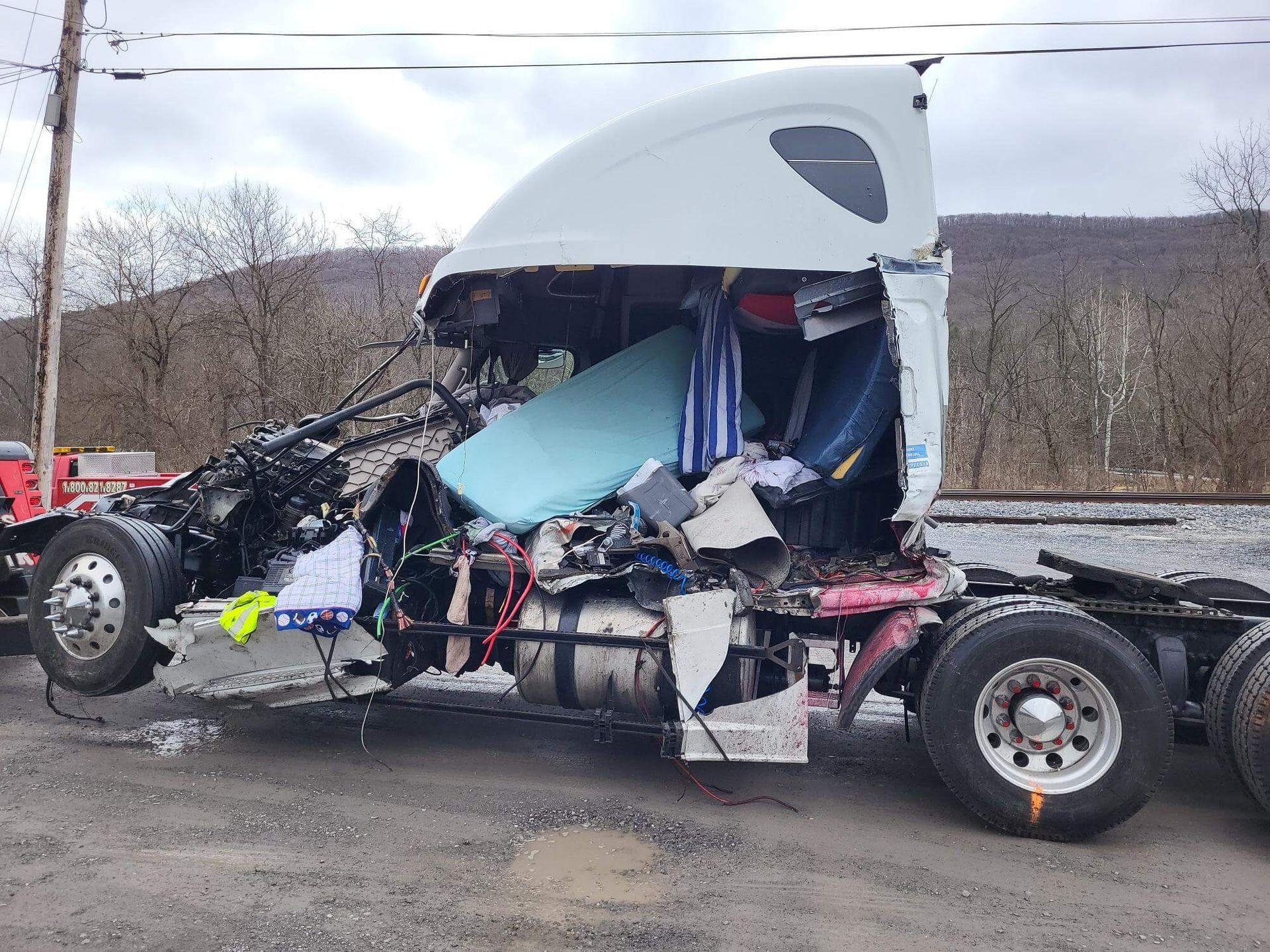 Severely wrecked semi-truck cab with crushed front end on a roadside in winter