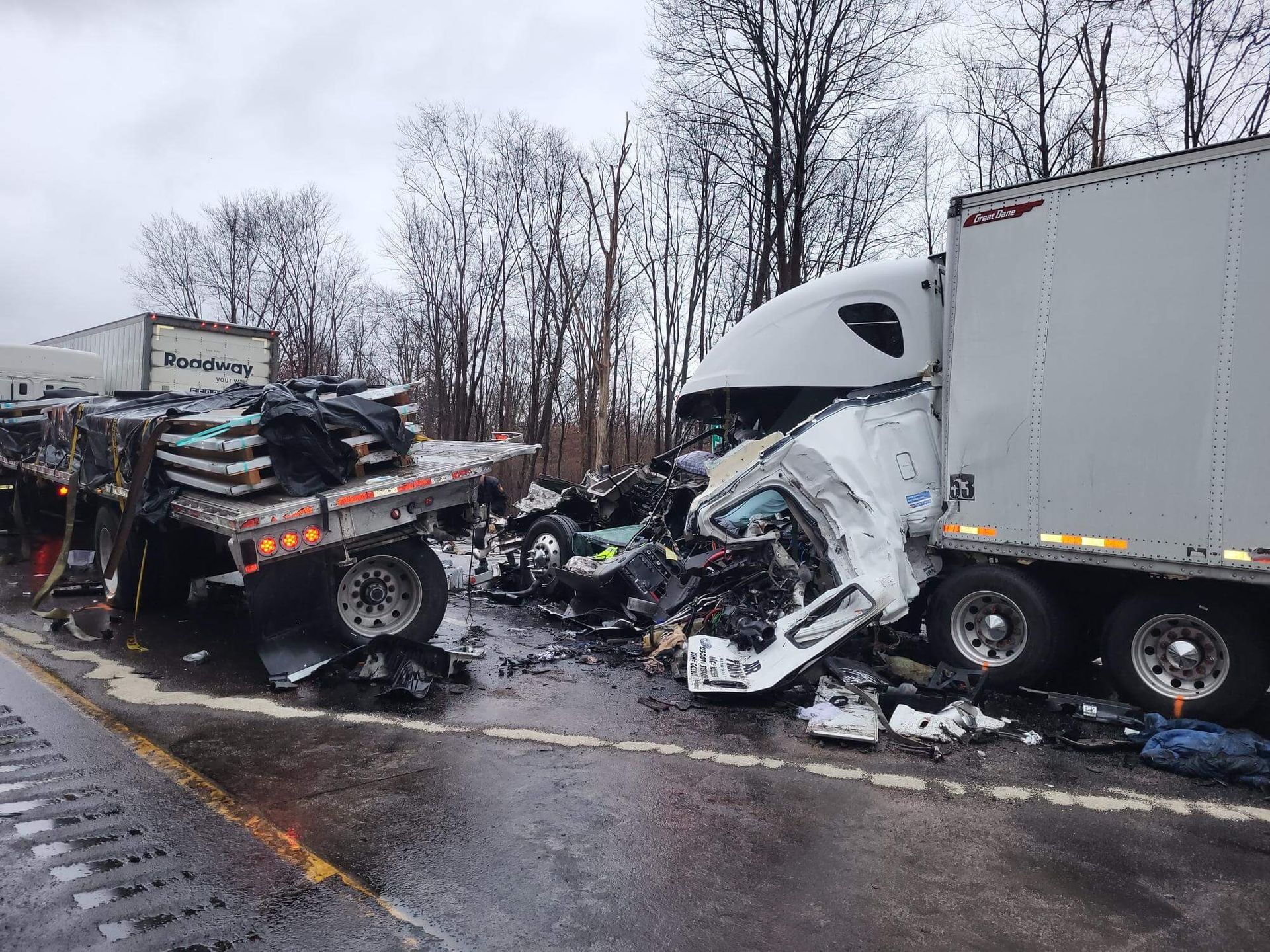 Severe highway crash with a mangled white semi-truck and a wrecked flatbed trailer amid debris and snow.