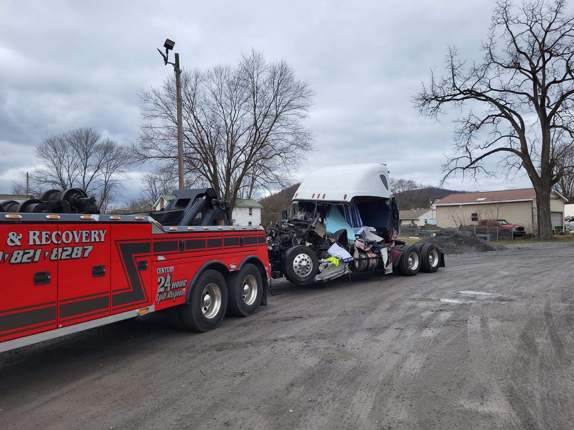 Tow truck hauling a crashed motorcycle in a muddy lot under a gray sky
