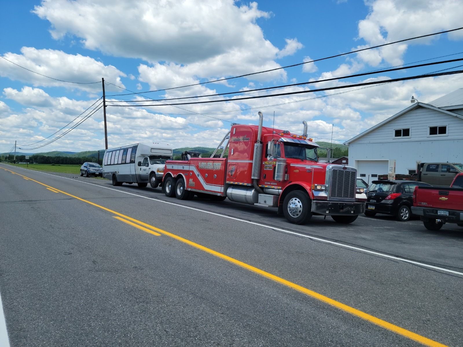 Red tow truck and white truck parked on roadside under a cloudy sky