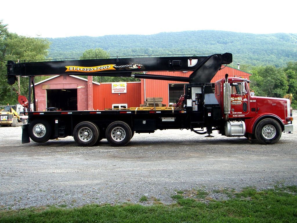 Red semi-truck with flatbed trailer parked in front of a red building.