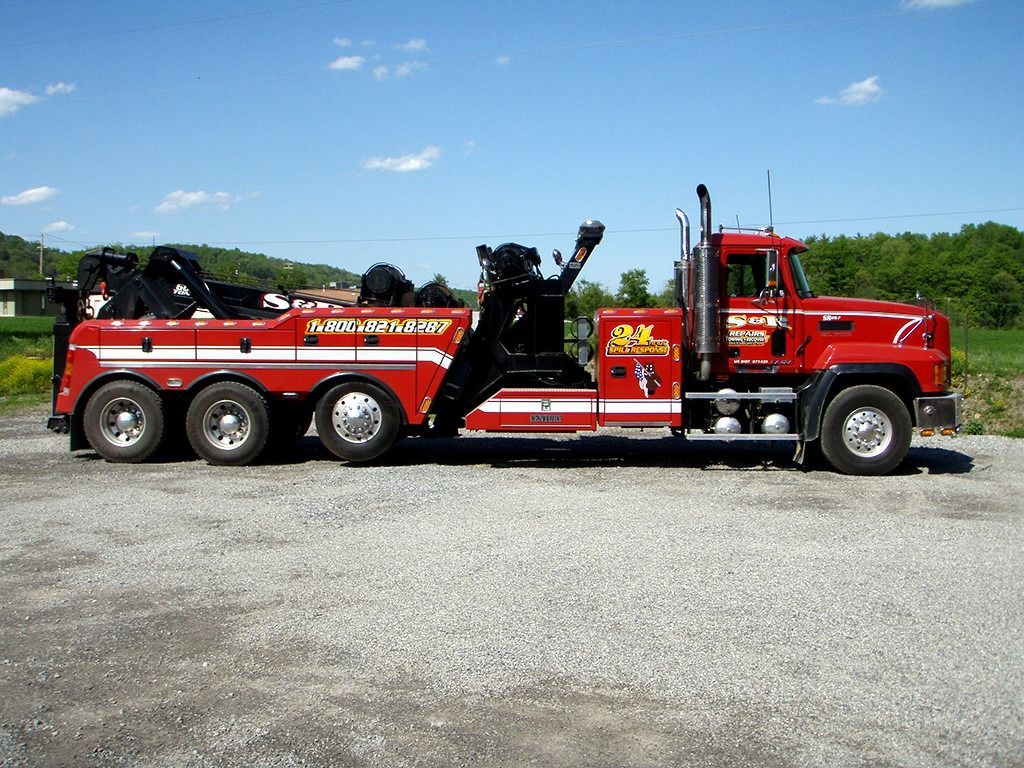 Red heavy-duty tow truck on gravel under a blue sky, side view with black equipment and red cab.