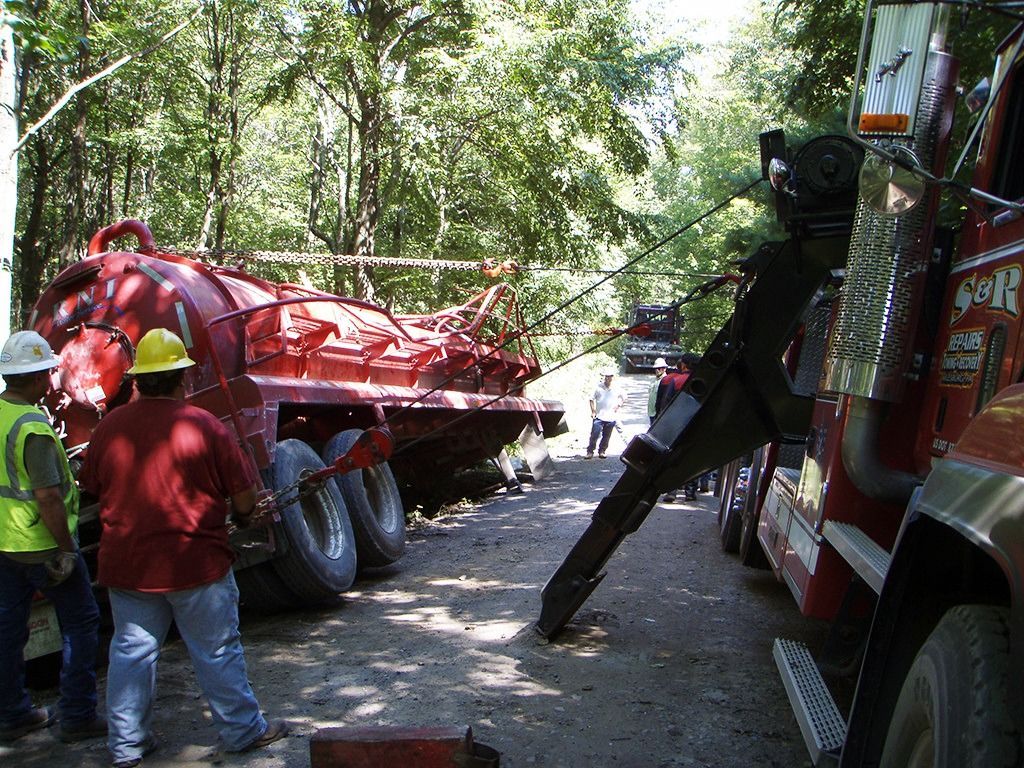 Emergency workers near a red truck in a wooded roadside accident scene
