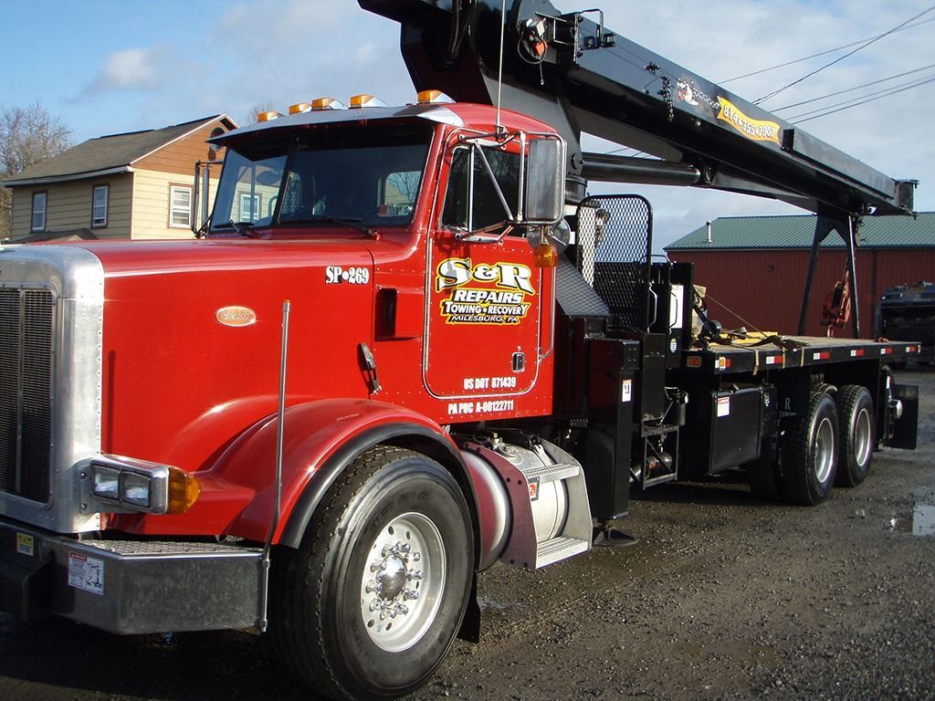 Red tow truck with black crane parked outdoors on gravel lot
