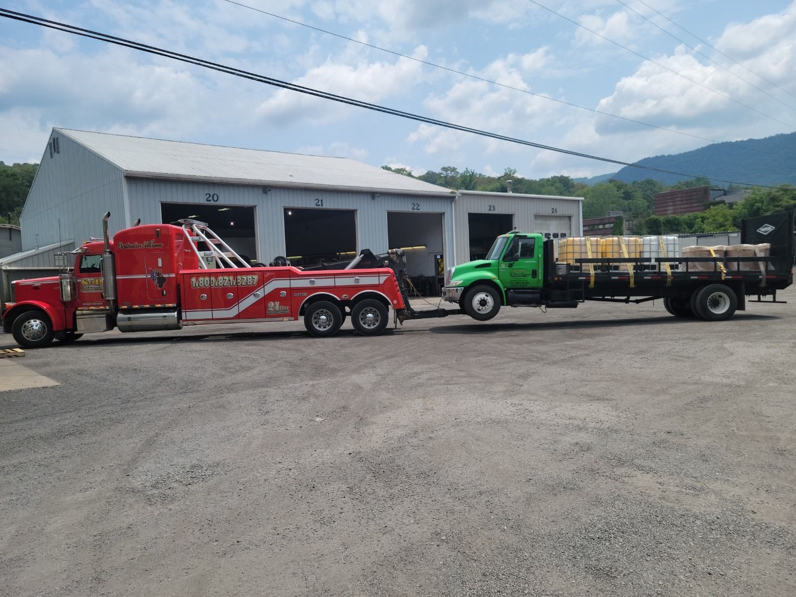 Red and green tow trucks parked outside a white garage on a gravel lot under a cloudy sky