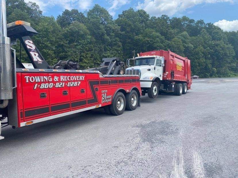 Red towing and recovery truck hauling a white dump truck on a roadside