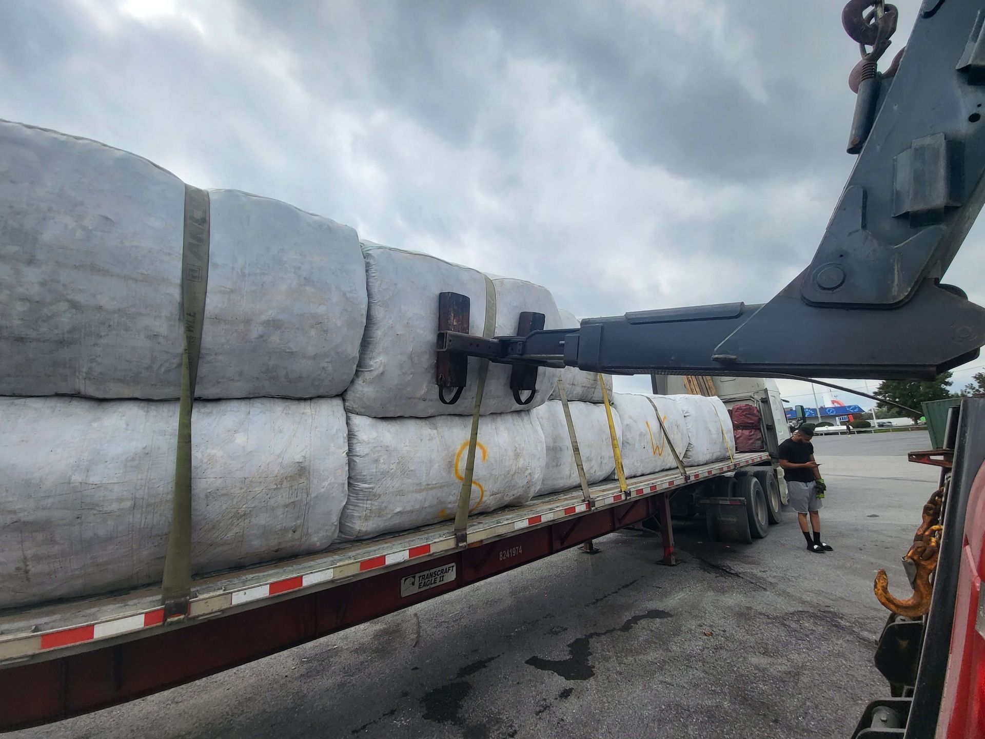 Heavy white sacks loaded on a flatbed truck, secured with straps, with a forklift lifting at a warehouse.