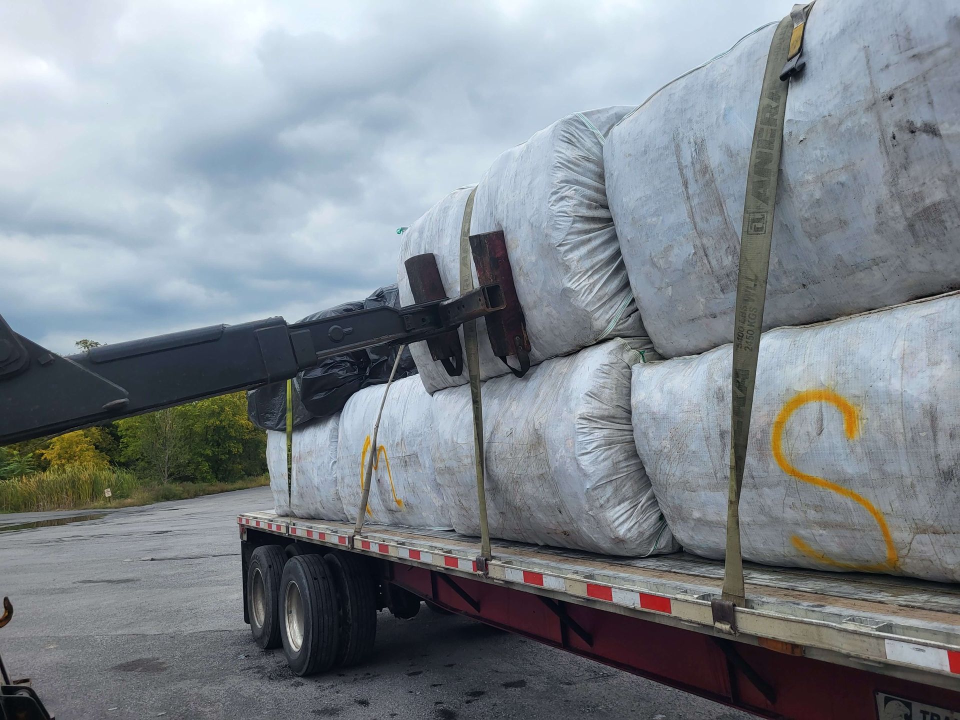 Flatbed trailer carrying large white wrapped bundles secured with straps on a roadside.