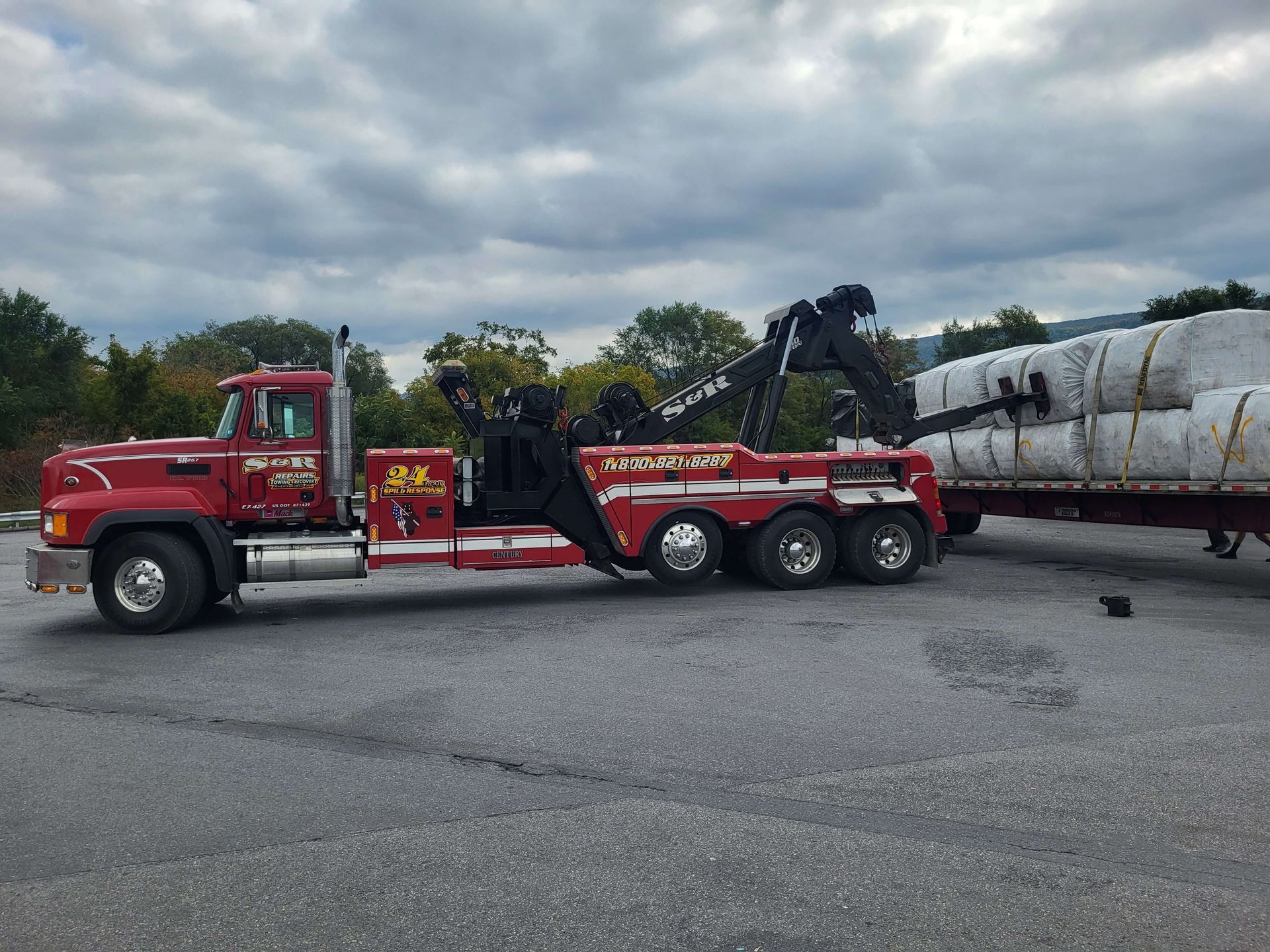 Red semi truck hauling long concrete pipes on a flatbed in a cloudy parking lot