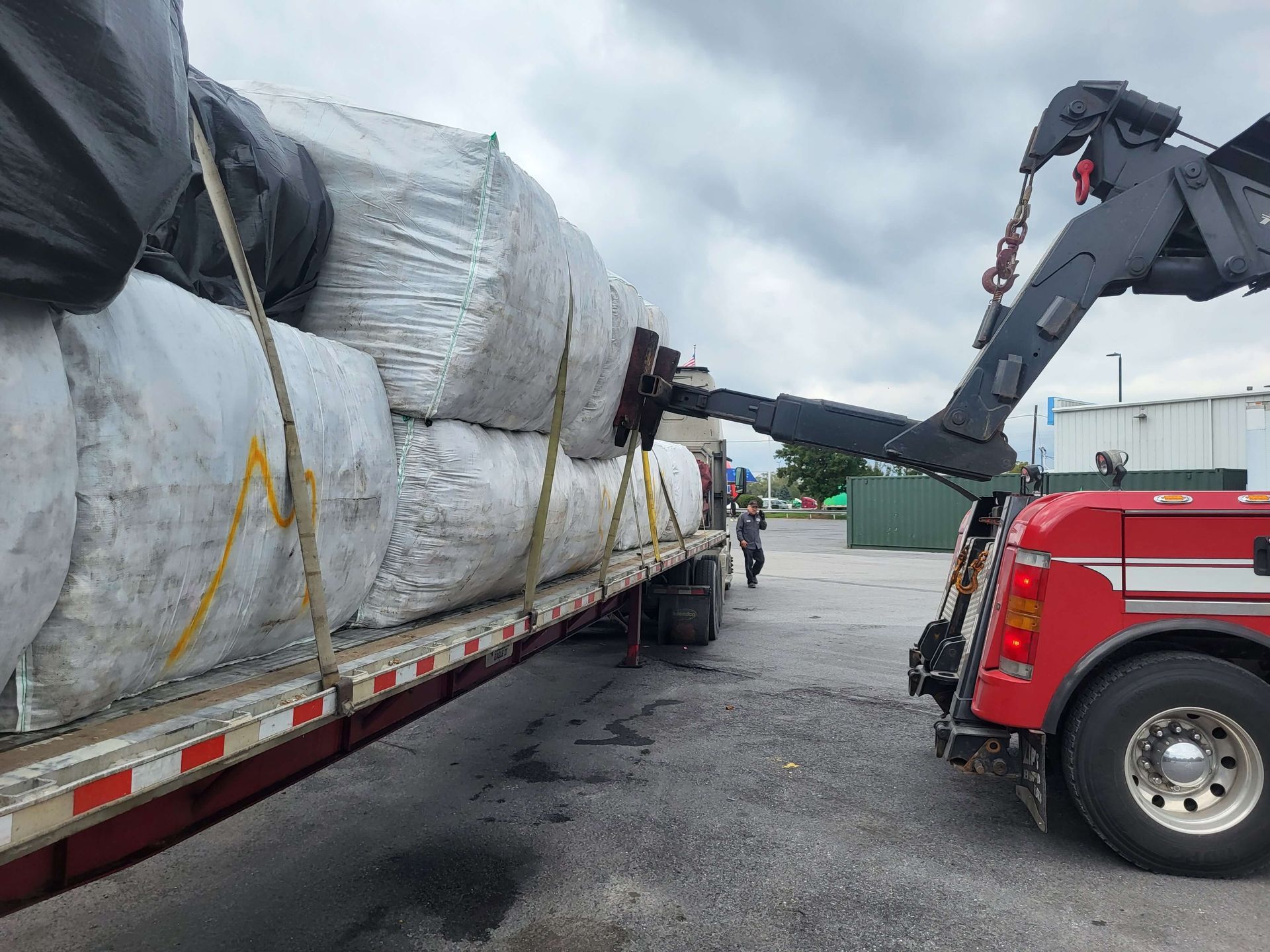 Tow truck loading a large wrapped trailer onto a flatbed on a wet lot