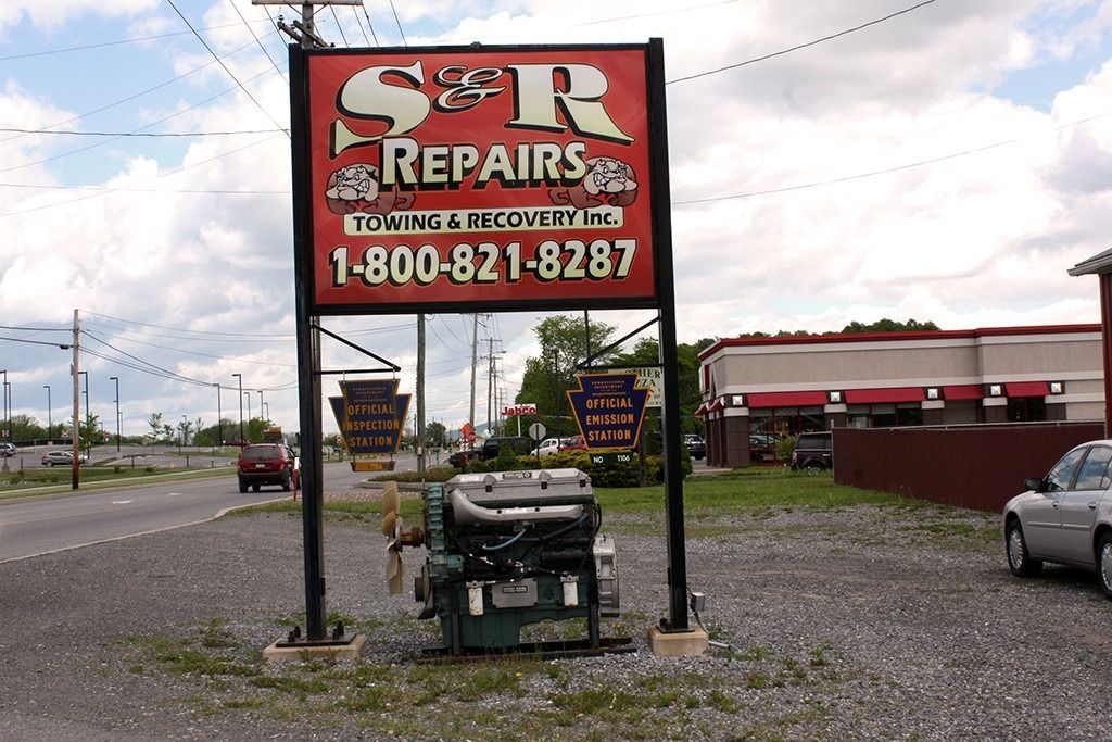 S&R Repairs roadside sign above a gravel lot with a green trash bin and parked cars under cloudy skies