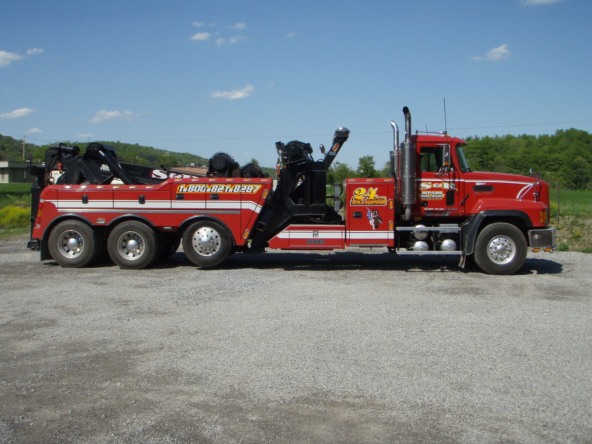 Red tow truck with black lifting apparatus parked on gravel under a blue sky
