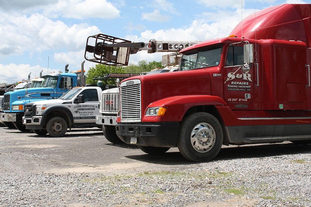 Row of parked semi trucks, including a red truck in front, on a gravel lot under a blue sky.