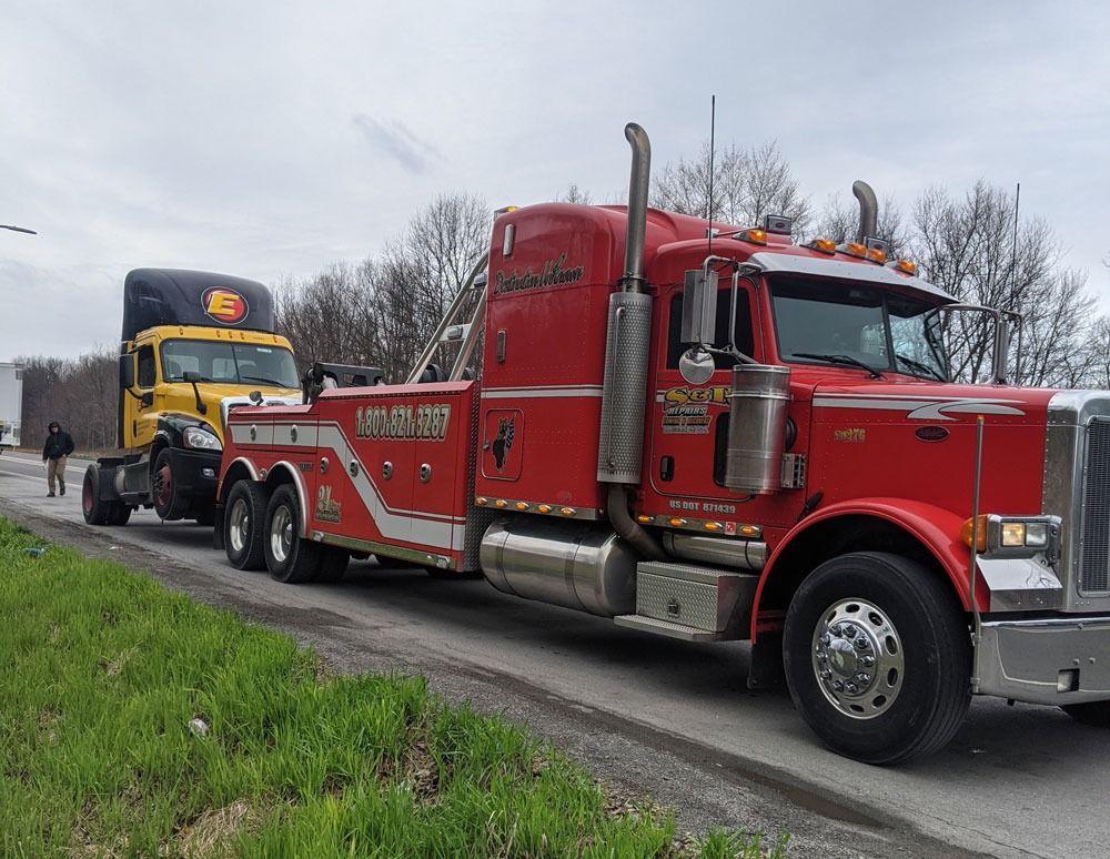 Red tow truck hauling a yellow bus on a roadside under cloudy skies