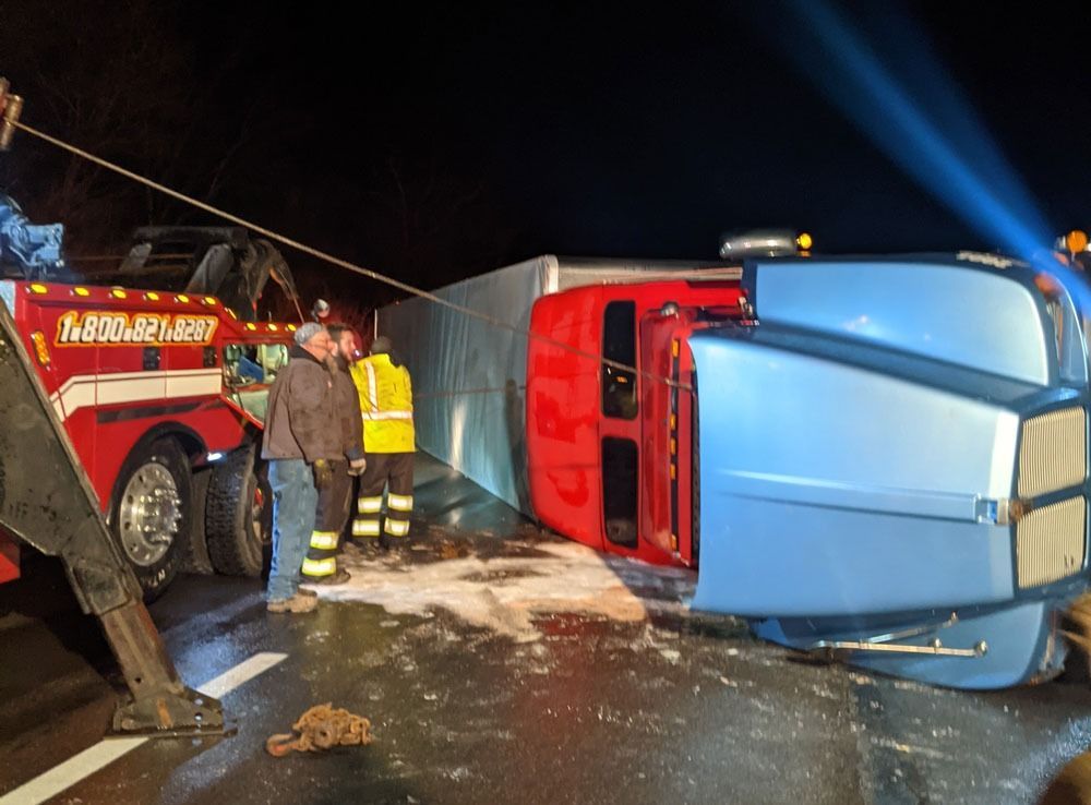 Overturned blue van beside red tow truck at night, with responders on a snowy road