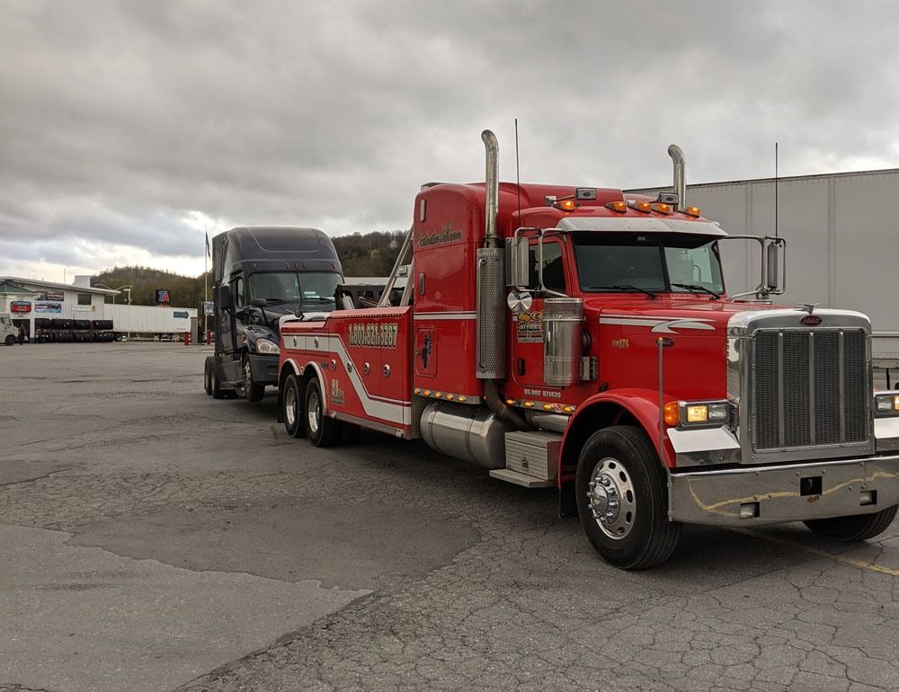 Red semi-truck hauling a black car carrier trailer in an industrial lot under cloudy skies