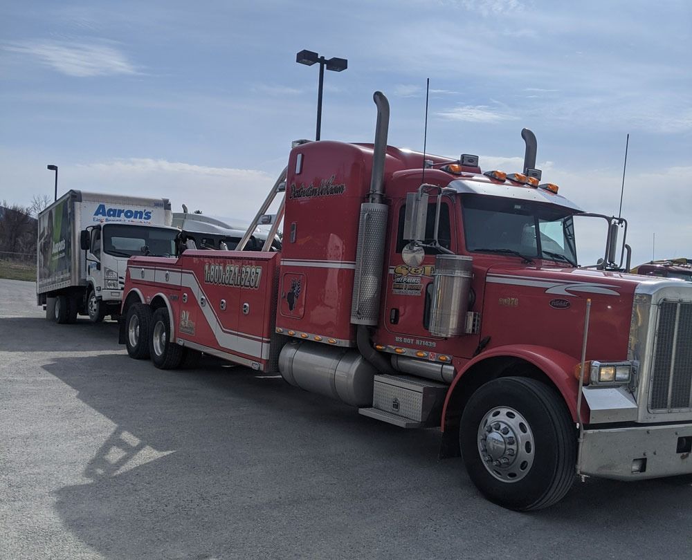 Red semi-truck towing a white box trailer in a parking lot on a cloudy day
